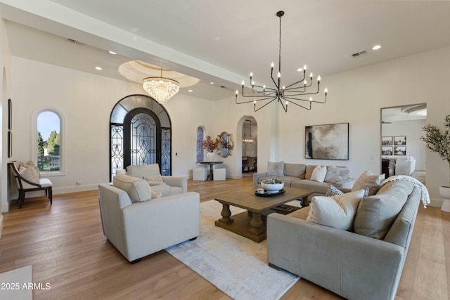 living room featuring a chandelier, arched walkways, visible vents, and light wood finished floors