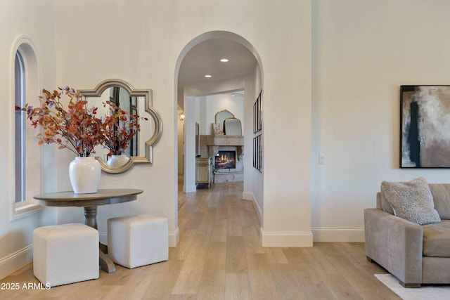 hallway with light wood finished floors, baseboards, arched walkways, and recessed lighting