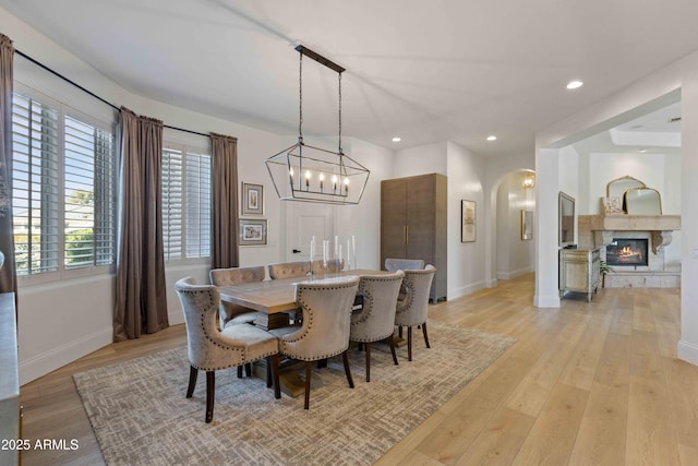 dining area with light wood finished floors, baseboards, arched walkways, a glass covered fireplace, and recessed lighting