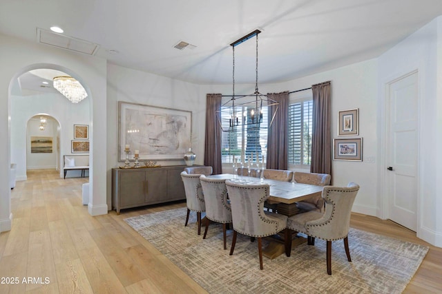 dining space featuring arched walkways, a notable chandelier, visible vents, baseboards, and light wood finished floors