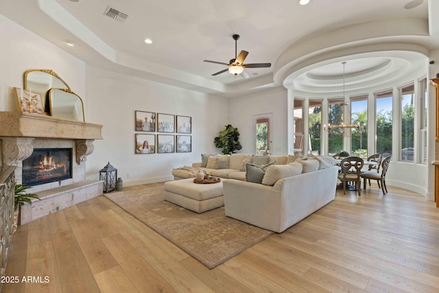 living room featuring baseboards, visible vents, a premium fireplace, hardwood / wood-style floors, and a tray ceiling