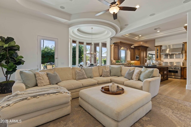 living room featuring ceiling fan, light wood-type flooring, a raised ceiling, and recessed lighting