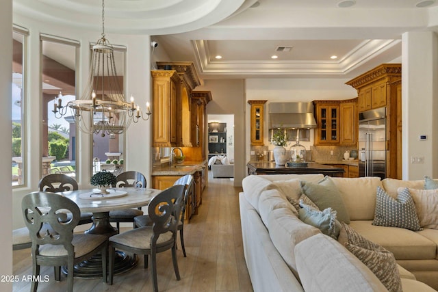 dining area with a notable chandelier, a raised ceiling, visible vents, light wood-style floors, and ornamental molding