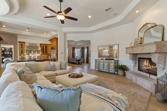 living area featuring a tray ceiling, recessed lighting, visible vents, light wood-style floors, and a high end fireplace