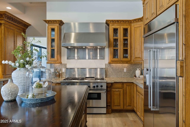 kitchen featuring wall chimney range hood, high quality appliances, and brown cabinetry