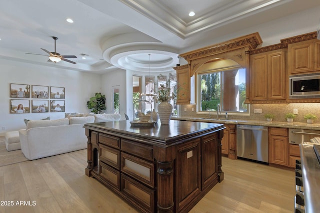 kitchen with stainless steel appliances, tasteful backsplash, a raised ceiling, light wood-style floors, and a sink