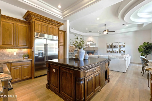 kitchen with decorative backsplash, a raised ceiling, a lit fireplace, stainless steel built in refrigerator, and light wood-style floors