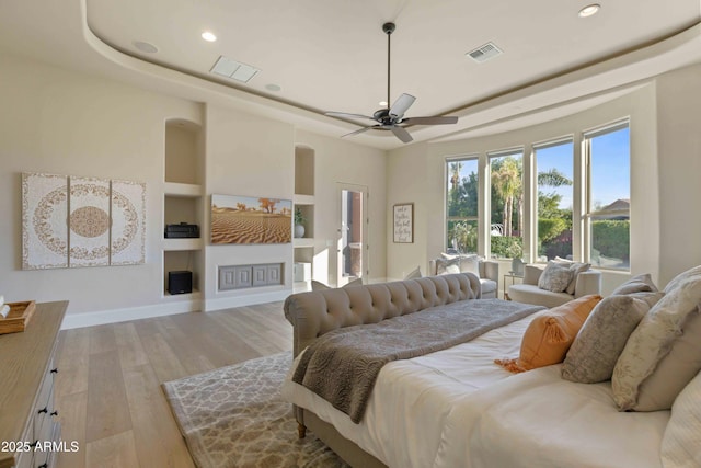 bedroom with baseboards, visible vents, a raised ceiling, and wood finished floors