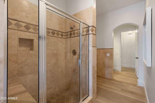 bathroom featuring a stall shower, baseboards, tile walls, and wood finished floors