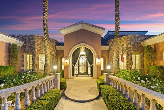 entrance to property with a tiled roof, stone siding, and stucco siding