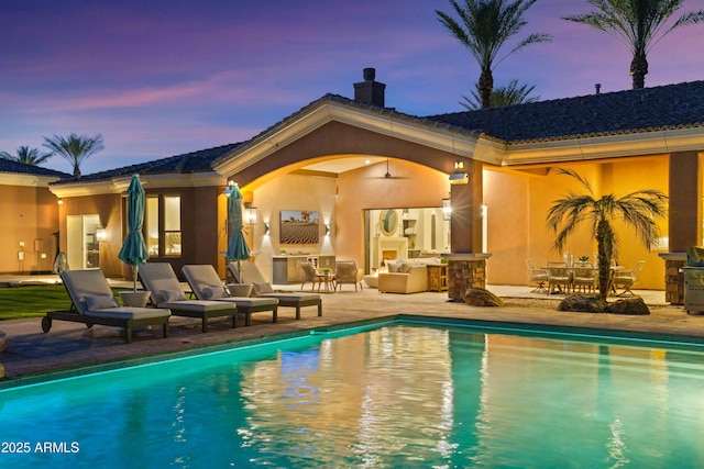 pool at dusk featuring a patio area, an outdoor pool, and a ceiling fan