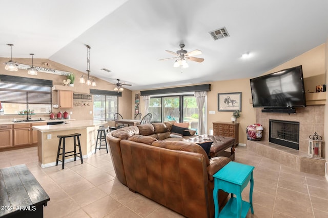 living room featuring lofted ceiling, sink, a tiled fireplace, and light tile patterned floors