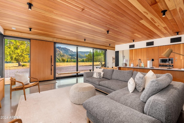 living room with a mountain view, wooden ceiling, sink, and a wall of windows