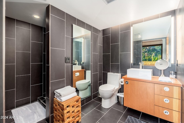 bathroom with toilet, vanity, tile patterned floors, and tile walls