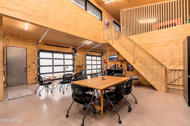 dining space featuring a towering ceiling, concrete floors, and wooden walls