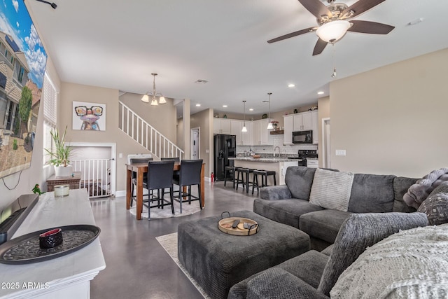 living area with finished concrete flooring, ceiling fan with notable chandelier, recessed lighting, baseboards, and stairway