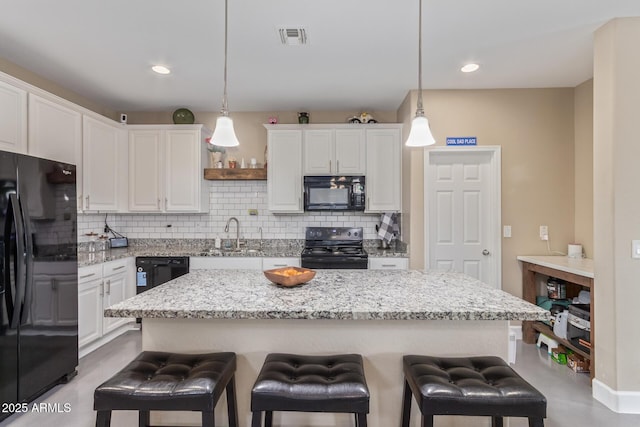 kitchen featuring visible vents, a breakfast bar, black appliances, and tasteful backsplash