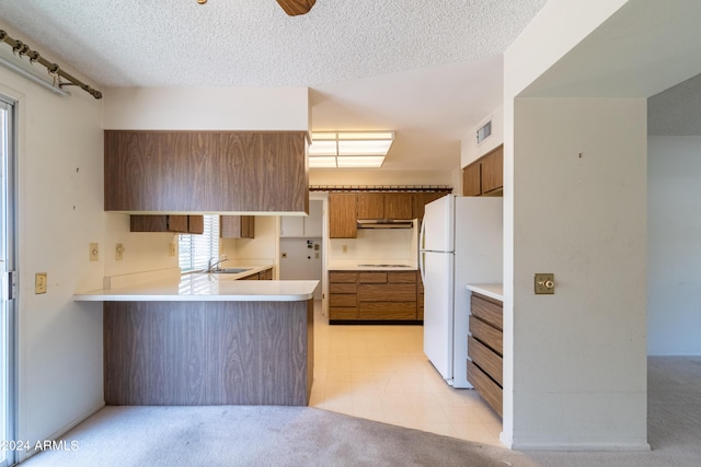 kitchen featuring sink, white refrigerator, kitchen peninsula, a textured ceiling, and cooktop