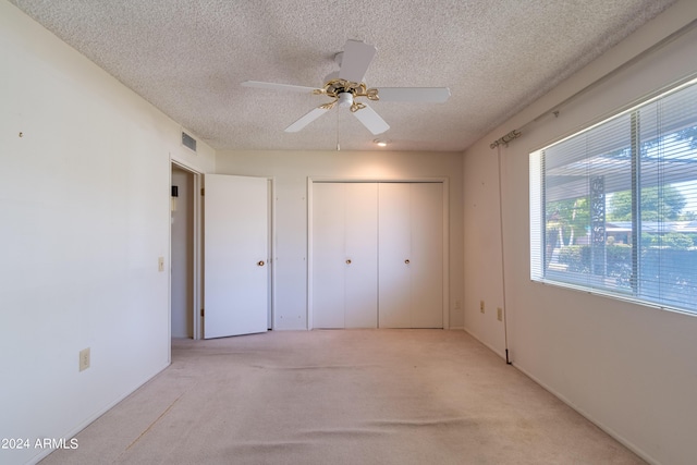 unfurnished bedroom with ceiling fan, a closet, light carpet, and a textured ceiling