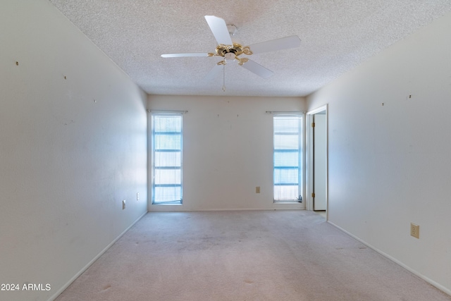 empty room featuring light carpet, ceiling fan, a wealth of natural light, and a textured ceiling