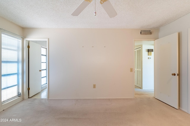 spare room with ceiling fan, a wealth of natural light, light colored carpet, and a textured ceiling