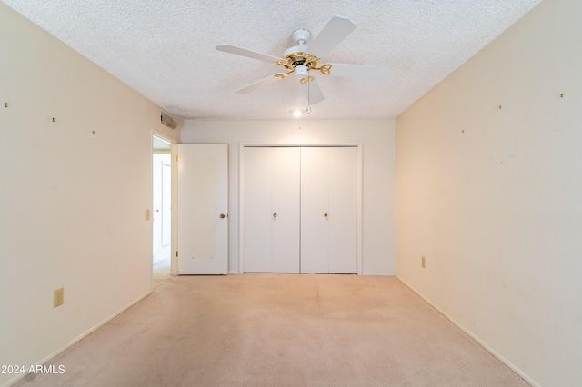 unfurnished bedroom featuring ceiling fan, light colored carpet, a closet, and a textured ceiling