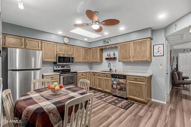 kitchen with sink, ceiling fan, a skylight, stainless steel appliances, and wood-type flooring