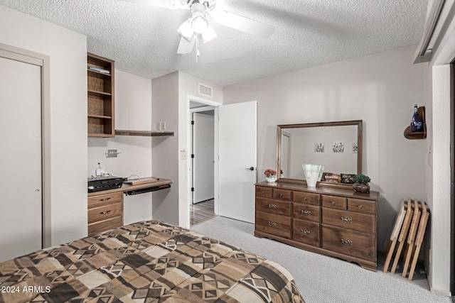 carpeted bedroom featuring ceiling fan, built in desk, and a textured ceiling