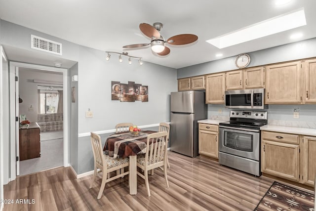 kitchen with a skylight, stainless steel appliances, light brown cabinetry, and light wood-type flooring