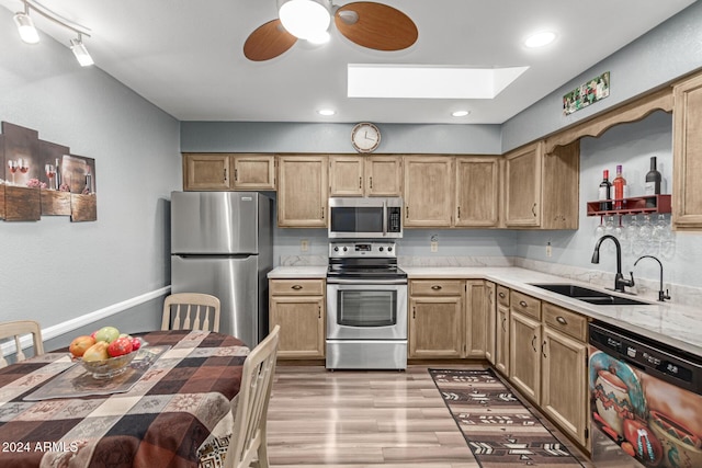 kitchen with appliances with stainless steel finishes, a skylight, sink, ceiling fan, and light hardwood / wood-style flooring