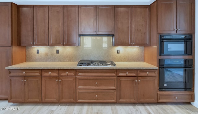 kitchen with stainless steel gas cooktop, extractor fan, light wood-type flooring, double oven, and backsplash