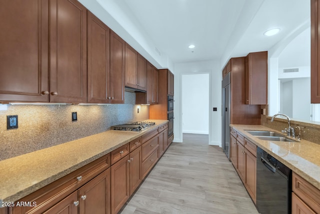 kitchen featuring sink, light stone counters, light hardwood / wood-style flooring, decorative backsplash, and black appliances