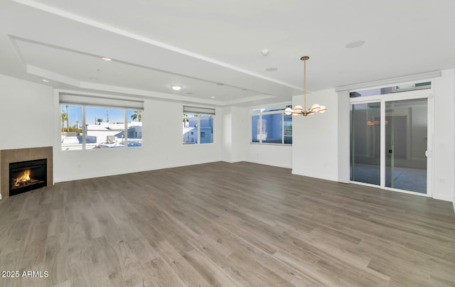 unfurnished living room with a tiled fireplace, a chandelier, a raised ceiling, and hardwood / wood-style floors