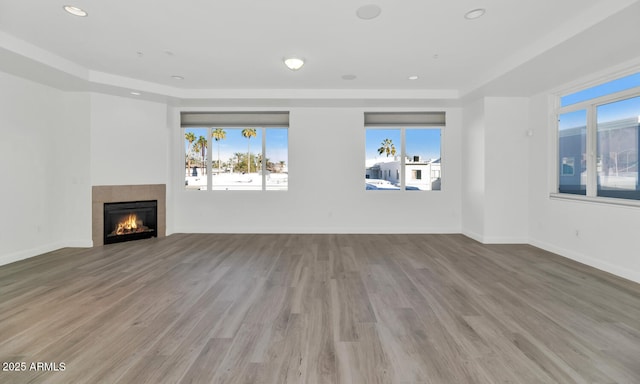 unfurnished living room with plenty of natural light, a tray ceiling, light hardwood / wood-style floors, and a tile fireplace