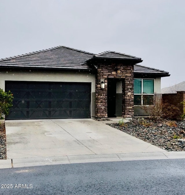 prairie-style home featuring stone siding, stucco siding, concrete driveway, and a garage