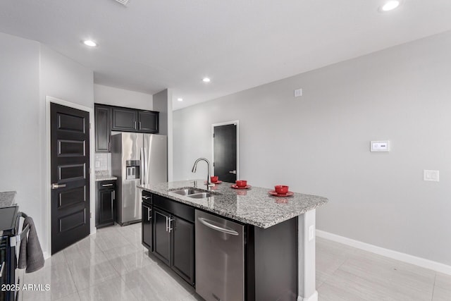 kitchen with a kitchen island with sink, a sink, recessed lighting, stainless steel appliances, and light stone countertops