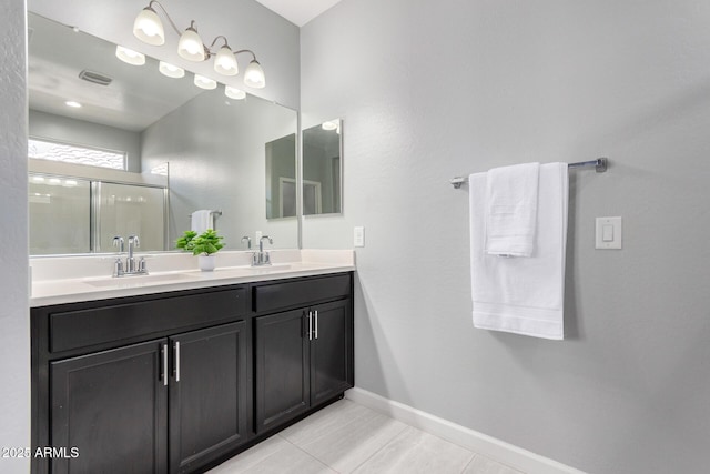 bathroom with a sink, baseboards, a shower with shower door, and double vanity