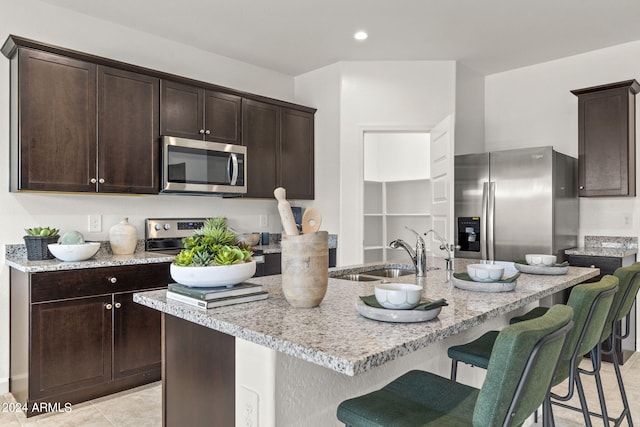 kitchen with sink, a breakfast bar area, dark brown cabinets, an island with sink, and stainless steel appliances