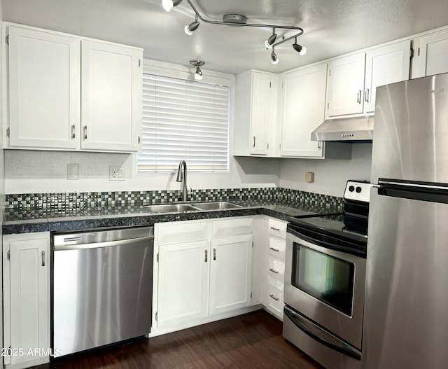 kitchen with dark countertops, appliances with stainless steel finishes, under cabinet range hood, white cabinetry, and a sink