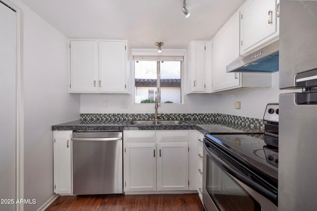 kitchen with dark countertops, appliances with stainless steel finishes, under cabinet range hood, white cabinetry, and a sink