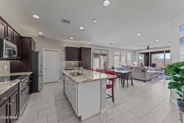 kitchen featuring ceiling fan, light stone countertops, an island with sink, tasteful backsplash, and stainless steel appliances