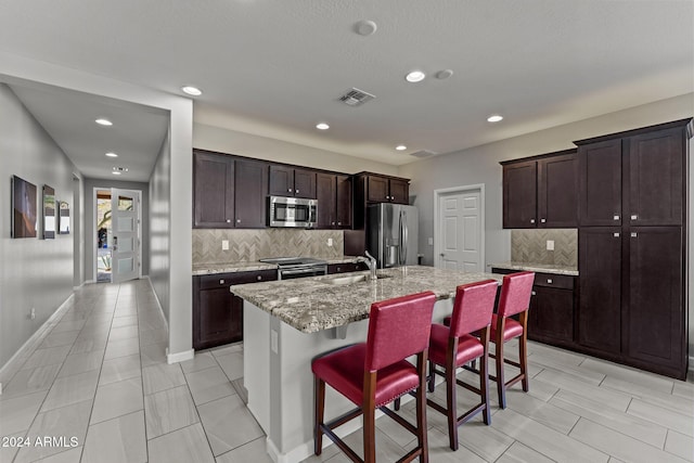 kitchen with a kitchen breakfast bar, a kitchen island with sink, tasteful backsplash, and appliances with stainless steel finishes