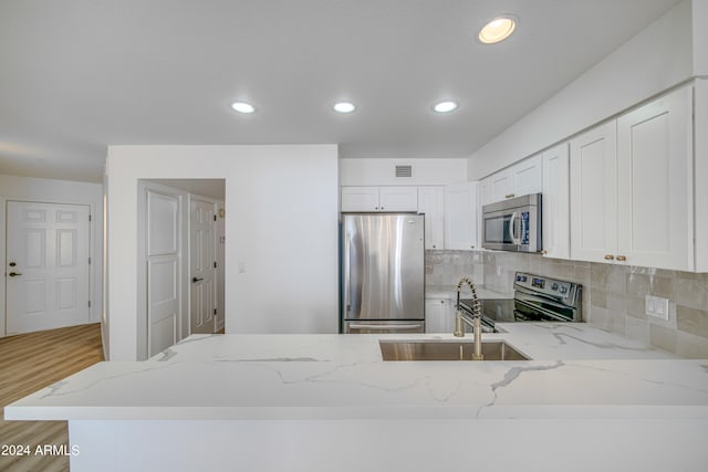 kitchen with stainless steel appliances, white cabinetry, light wood-type flooring, and light stone counters