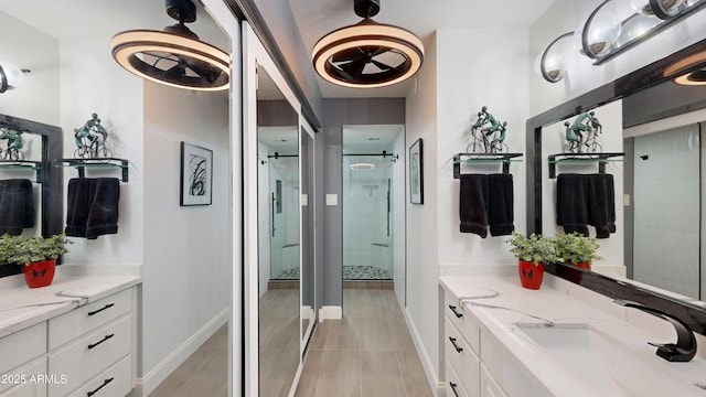 bathroom featuring a stall shower, baseboards, two vanities, and a sink