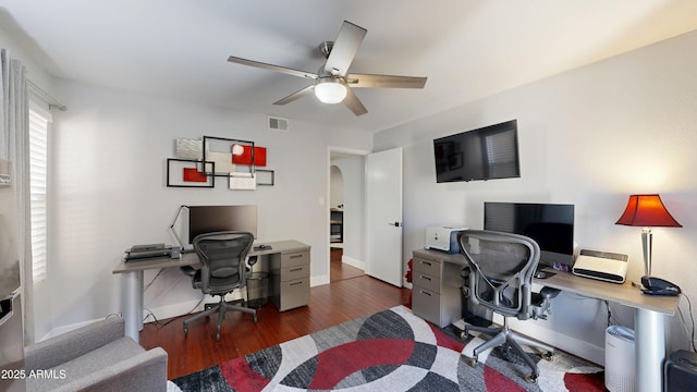 office with arched walkways, wood finished floors, visible vents, baseboards, and a ceiling fan