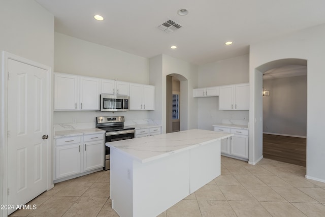 kitchen with light tile patterned floors, a kitchen island, light stone counters, white cabinetry, and stainless steel appliances