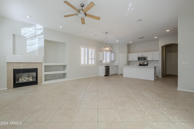 unfurnished living room with built in shelves, ceiling fan, a fireplace, and light tile patterned floors