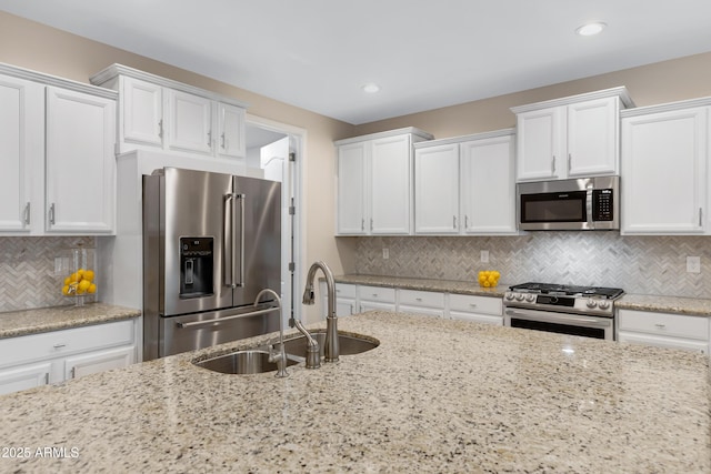 kitchen featuring sink, backsplash, stainless steel appliances, light stone counters, and white cabinets