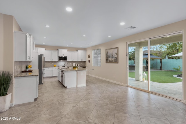 kitchen featuring appliances with stainless steel finishes, white cabinetry, light stone countertops, a center island with sink, and decorative backsplash