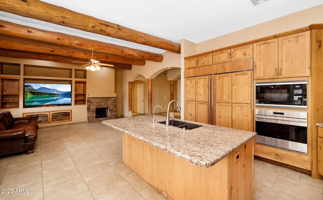 kitchen with light tile patterned floors, light stone counters, a kitchen island with sink, oven, and a sink